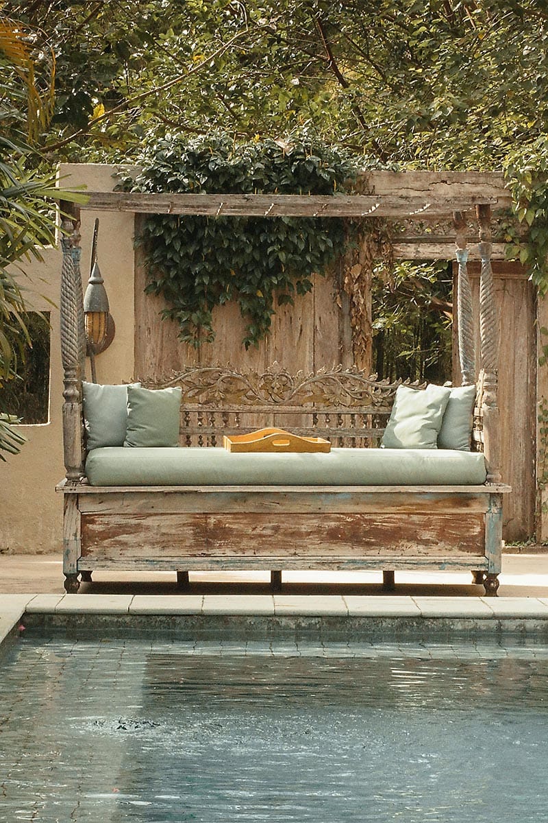 Rustic wooden daybed with soft cushions overlooking a serene pool, surrounded by tropical plants at Coquí Hideaway.